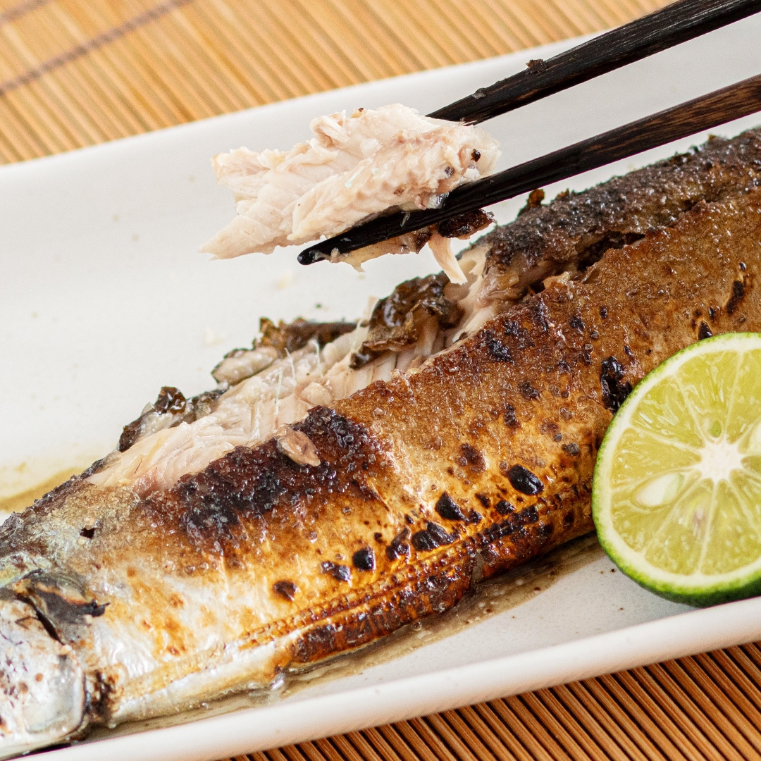 魚の塩焼きが白い皿に盛られ、箸で一口取られている。隣に半分に切られたライムが添えられている。