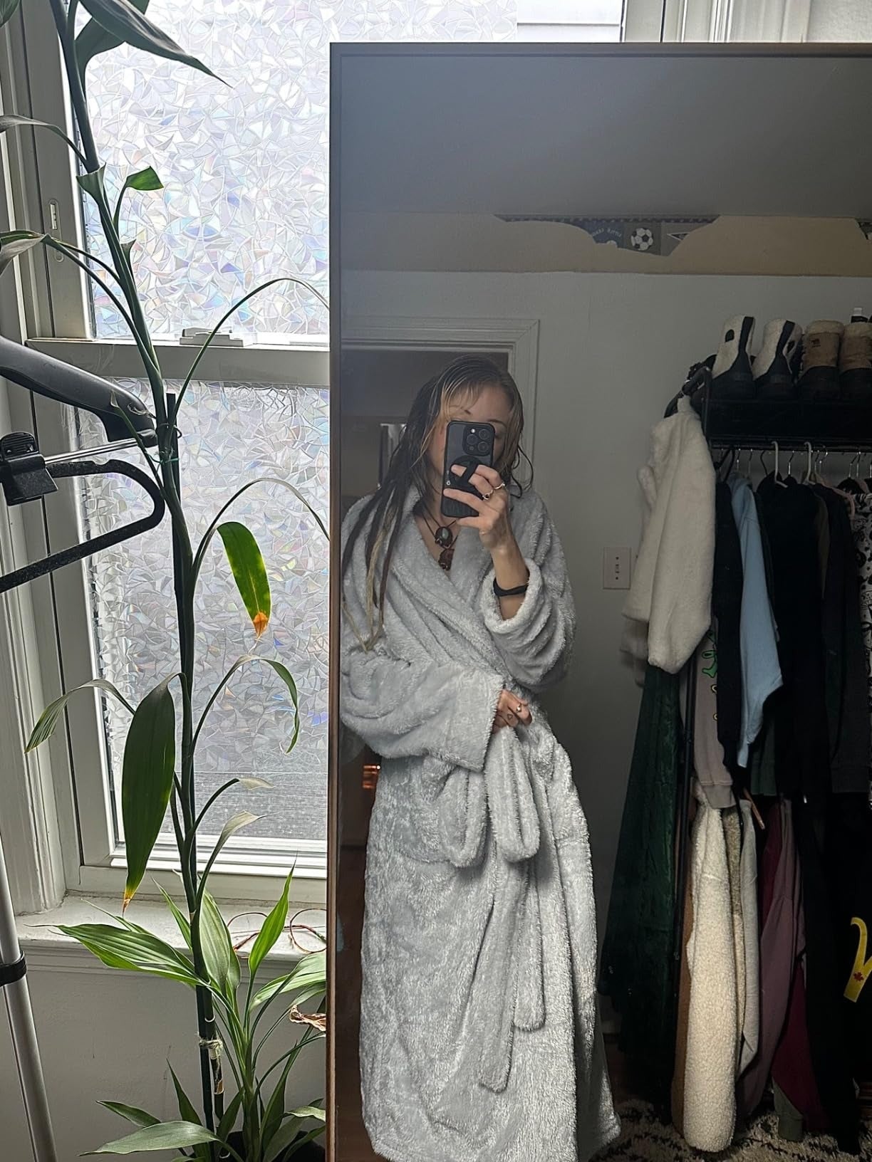 Person successful  a reflector  selfie wearing a plush robe stands adjacent   a works  and covering  rack, suggesting a comfy  location  buying  vibe