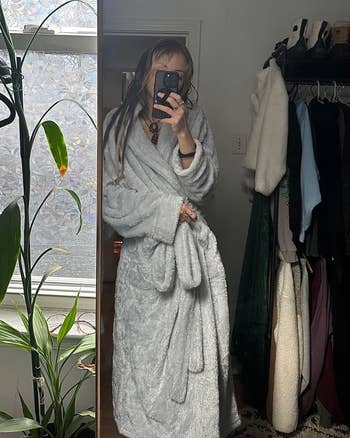 Person successful a reflector selfie wearing a plush robe stands adjacent a works and covering rack, suggesting a comfy location buying vibe