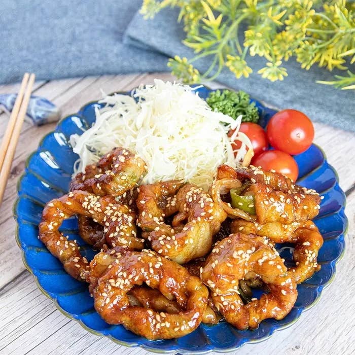 お皿に盛られた甘辛ソースの肉巻き、キャベツの千切り、ミニトマトの料理。