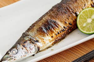 皿の上に盛り付けられた焼き魚と輪切りのライム、箸が置かれている。