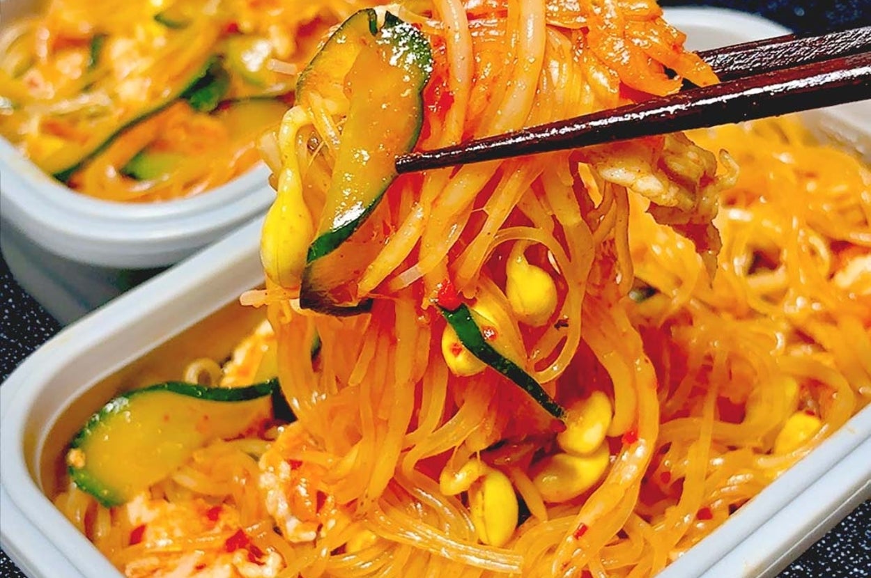 韓国風ビーフンを箸で持ち上げている場面。野菜と一緒にプラスチック容器に盛り付けられている。