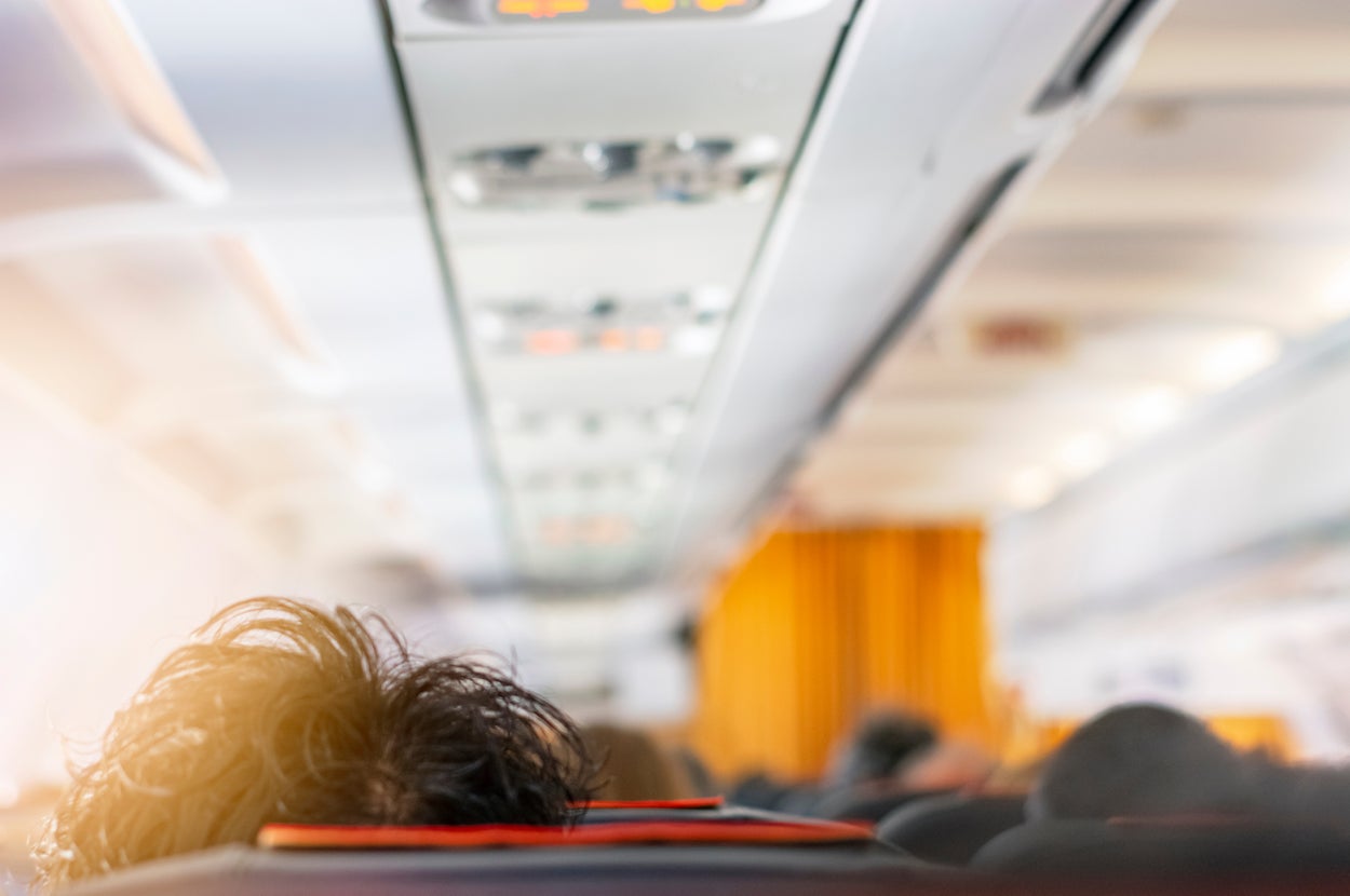 飛行機の客室内。乗客の頭越しに見える座席とオーバーヘッドコンパートメント。