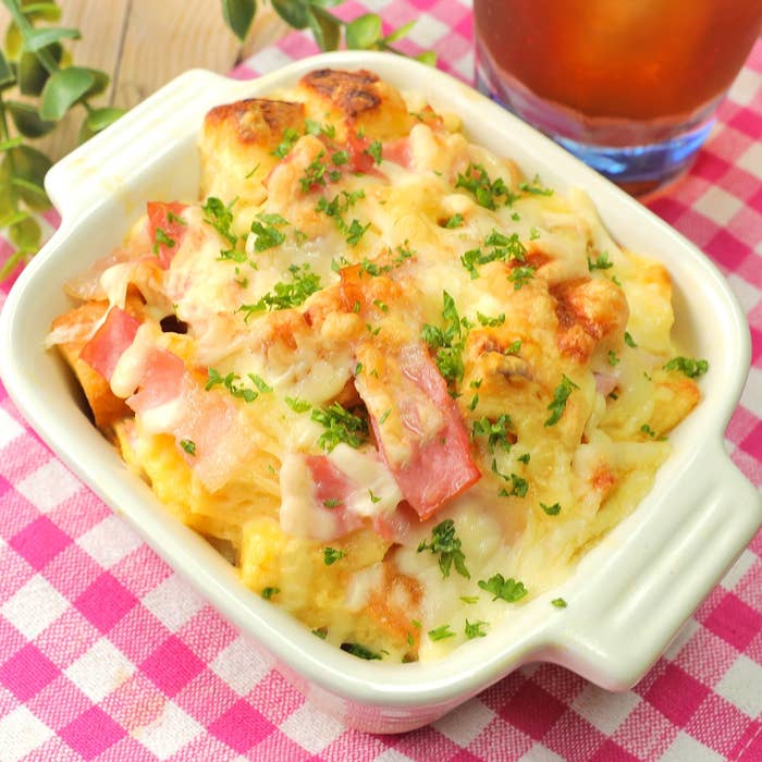 オーブン皿に焼かれたグラタン、ハムとチーズでトッピングされています。背景に飲み物が見えます。