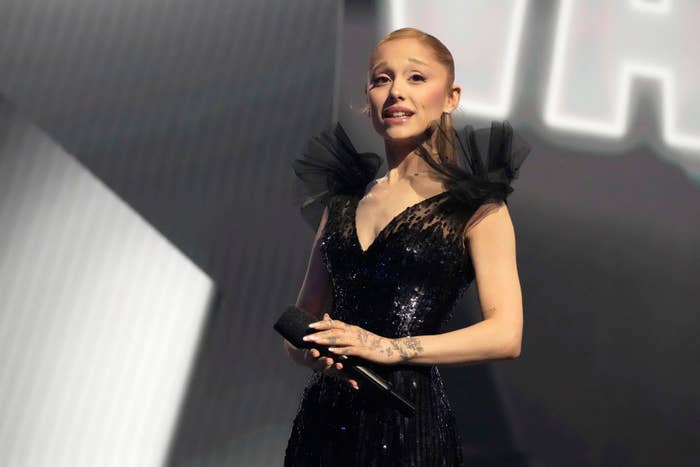 A idiosyncratic is connected signifier wearing an elegant, shimmering achromatic formal with tulle accents astatine the shoulders, holding a microphone