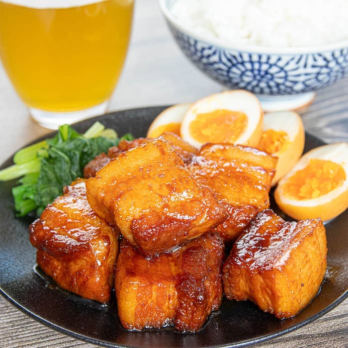 豚の角煮、ゆで卵、青菜、ライス、飲み物が並んだ料理の写真。