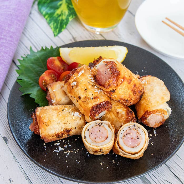 ソーセージがちくわで包まれた料理が皿に盛られ、横にトマトとレモンが添えられた美味しそうな食事。