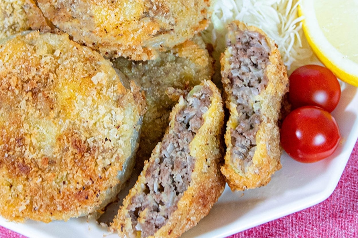 揚げたてのメンチカツが皿に盛られ、キャベツの千切り、レモン、ミニトマトが添えられている。後ろに玉ねぎが見える。