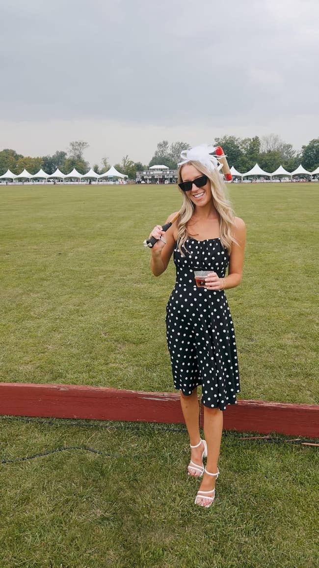 Person successful polka dot formal and achromatic fascinator holding a portion astatine an outdoor lawsuit with tents successful the background