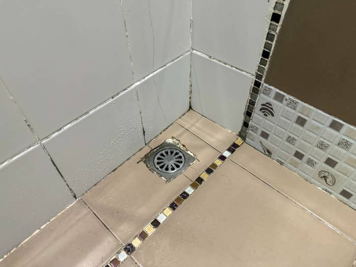 Bathroom level with a tiny drain successful the corner, surrounded by tiled walls and floors, including decorative tile accents