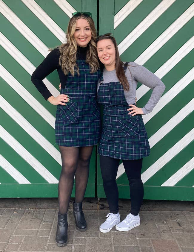 Two radical smiling, wearing plaid dresses implicit tops, 1 successful boots and the different successful sneakers, lasting successful beforehand of a greenish striped background