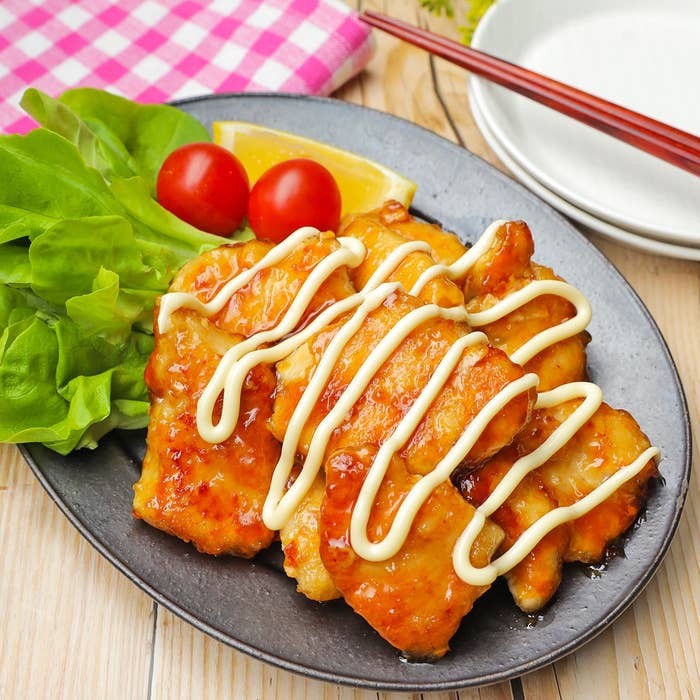 皿に乗ったチキン、マヨネーズがけ。レタス、プチトマト、レモン添え。食卓に並べられた料理。