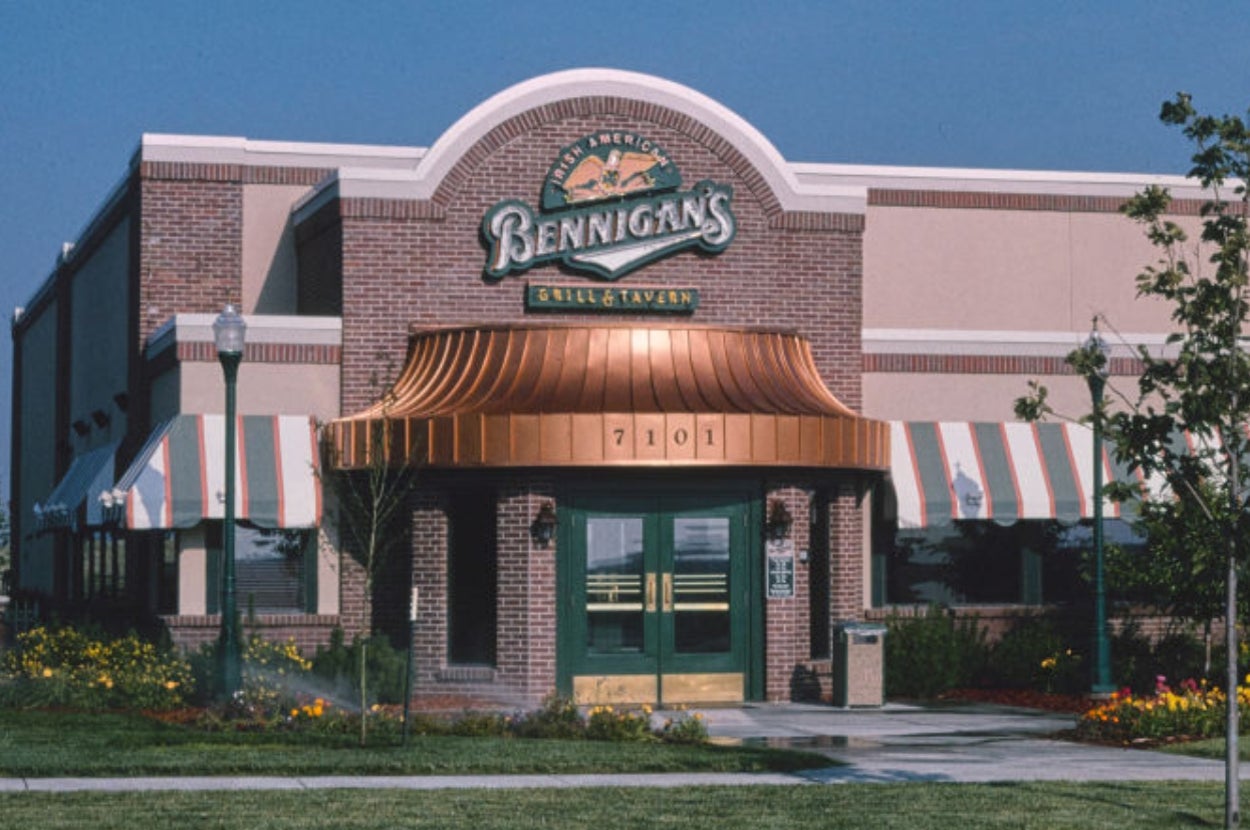 Bennigan's Grill & Tavern exterior with brick facade, arched windows, and striped awnings, surrounded by garden landscaping