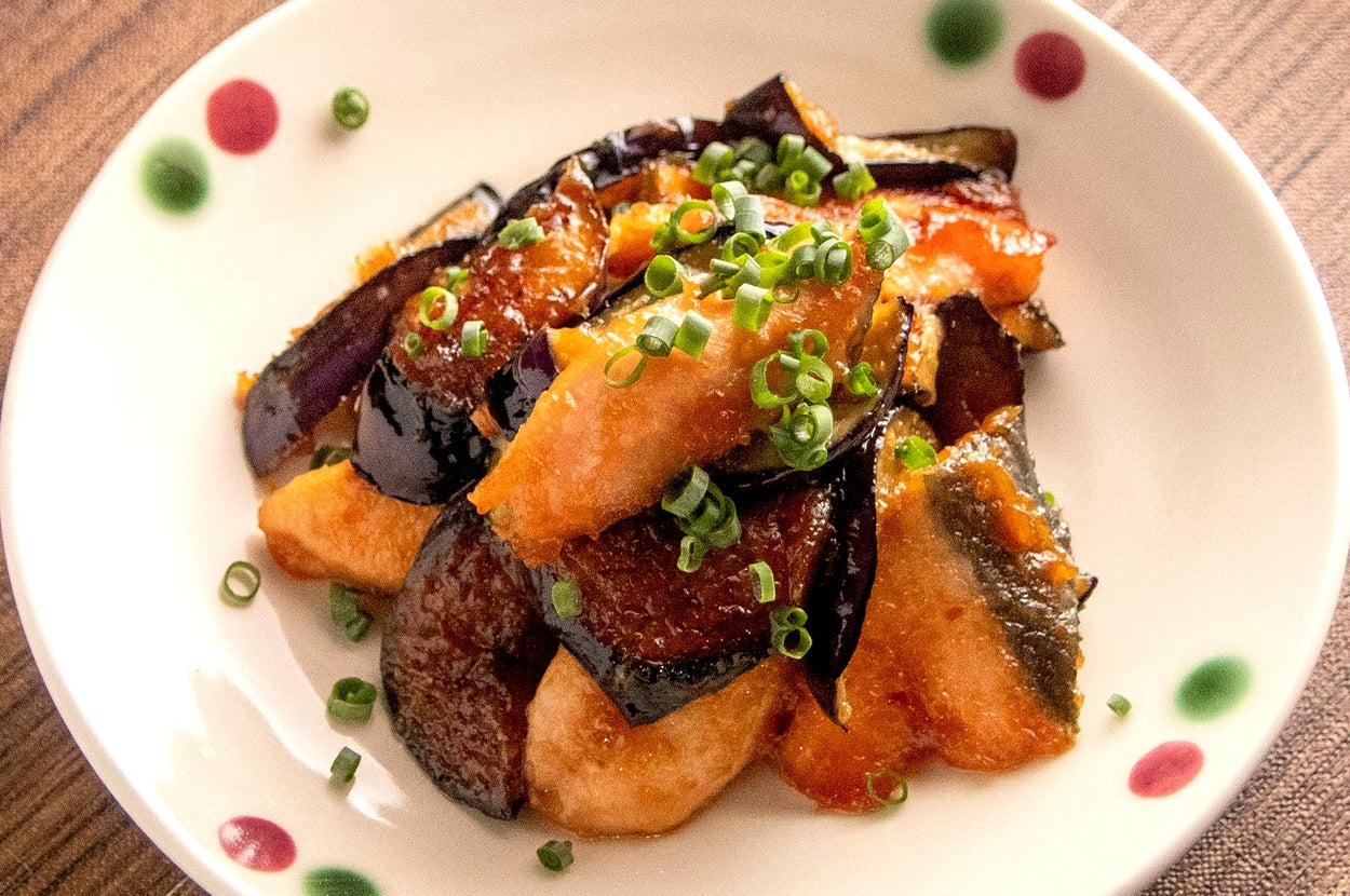鶏肉と茄子の料理が白い皿に盛られている。上に刻んだネギが散らされている。