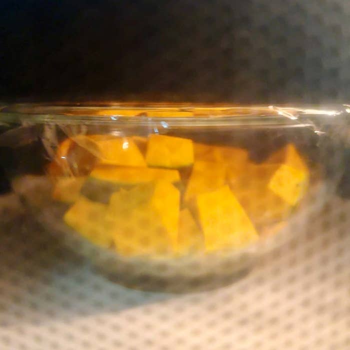電子レンジ内で加熱中の透明なボウルに入った角切りの食べ物。