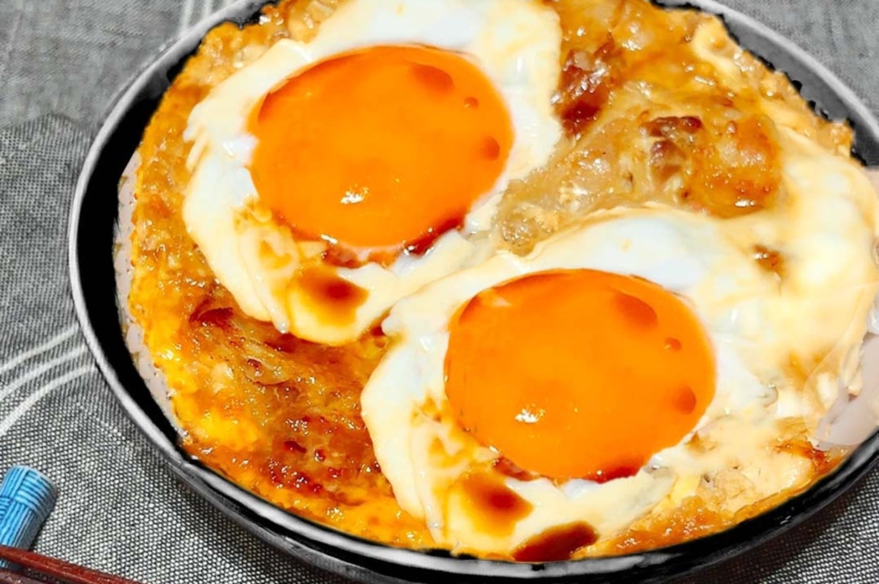 半熟卵がのった美味しそうな料理が盛られた黒いボウル、そばに箸が置かれている。