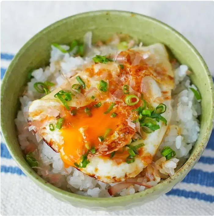 温かいご飯の上に目玉焼きとネギ、かつお節が載っているどんぶり料理。