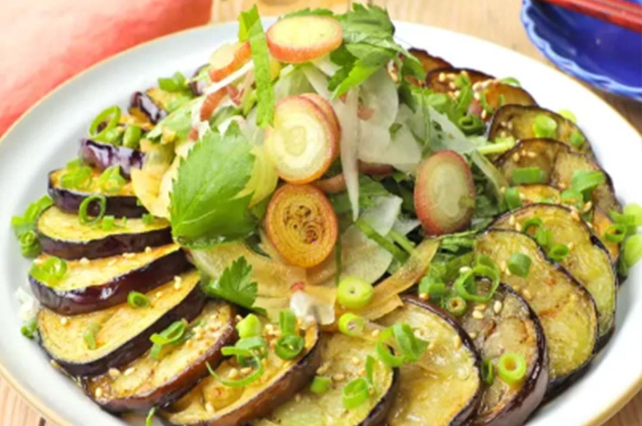 ナスのスライスとネギたっぷりの料理。中央にはハーブと薄切りの野菜がトッピングされ、カラフルでフレッシュな印象。