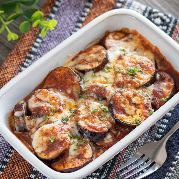 白い皿に盛られたチーズとソースをまとった焼き茄子の料理。フォークが横に置かれている。