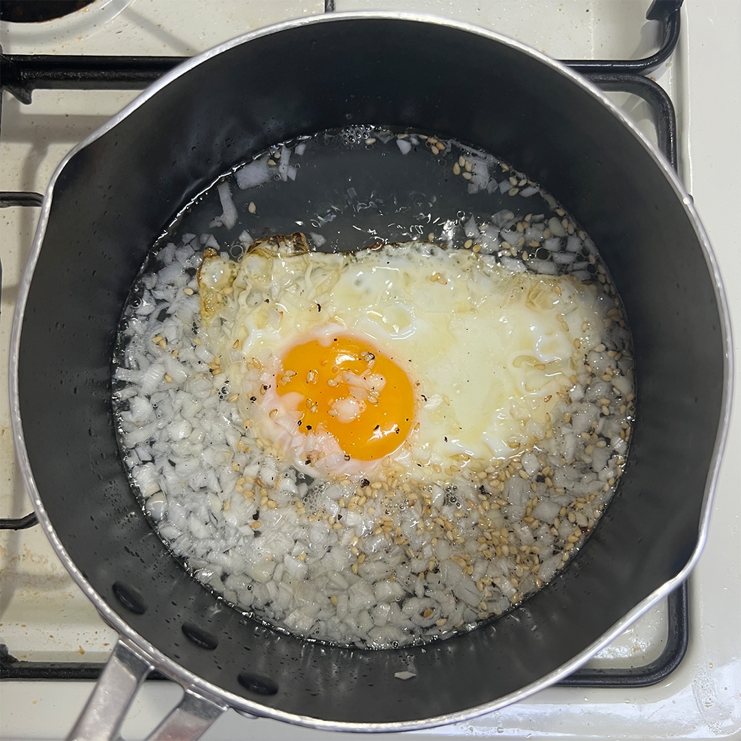 目玉焼きと刻んだ玉ねぎがフライパンで調理されています。