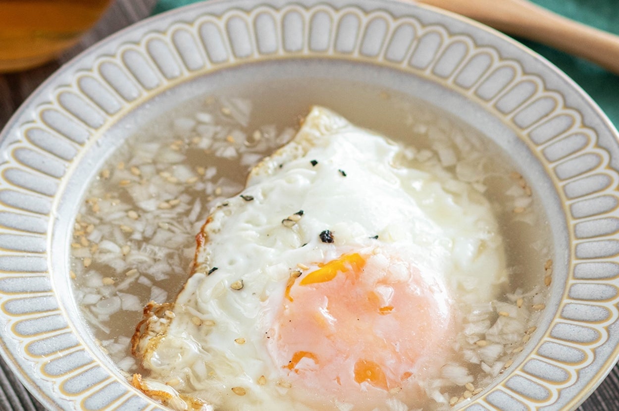 お粥の上に目玉焼きをのせた料理が皿に盛られ、木製スプーンと緑色の布が並んでいる。