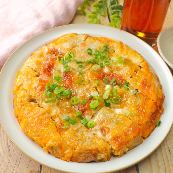 お好み焼きが皿に盛られており、ねぎがトッピングされています。隣にドリンクが置かれています。