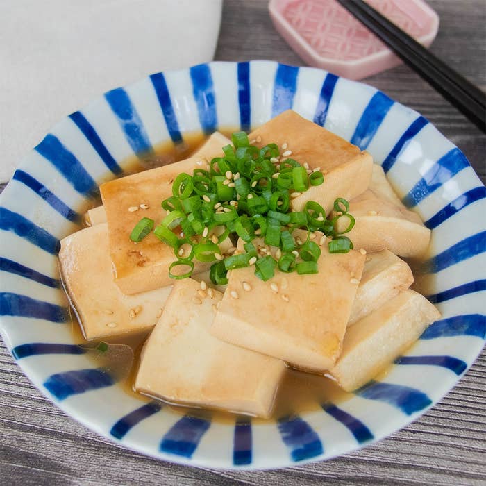 皿に盛られた豆腐料理。スライスし加熱された豆腐に小ネギと白いりごまがトッピングされ、たれがかかっている。