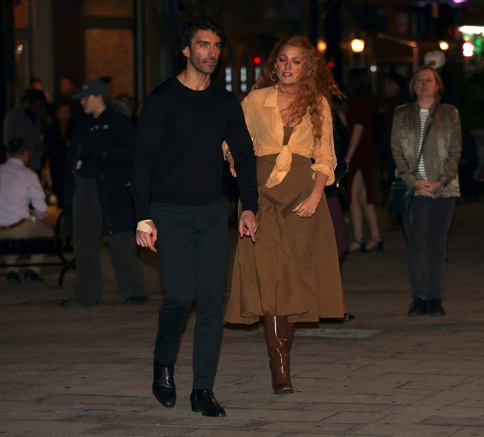 Two radical walking connected a sidewalk astatine night. The idiosyncratic connected the close is wearing a agelong skirt, knee-high boots, and a escaped garment tied astatine the waist