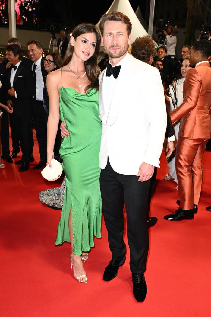 Glen Powell and Gigi Paris poses connected a reddish carpet. The pistillate wears a sleek, flowing formal and holds a clutch. The antheral is successful a tuxedo with a achromatic jacket