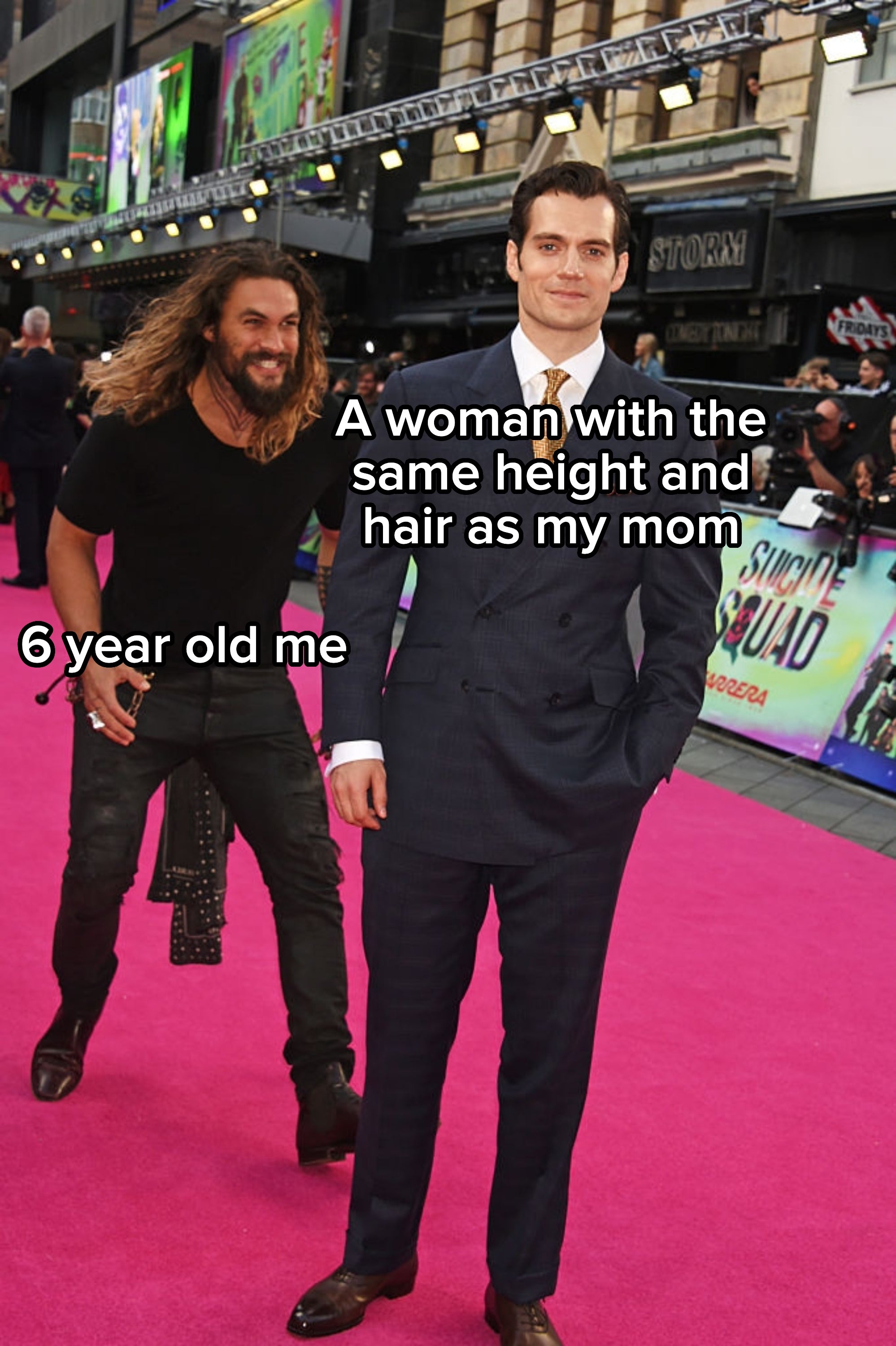Two men at a movie premiere. One in a formal suit, the other in a casual black outfit, having fun on a pink carpet