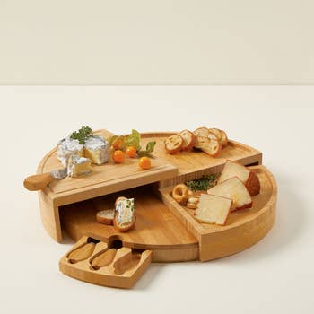 Round bamboo food committee with sliding drawer, food knives, assorted cheeses, breadstuff slices, and garnish