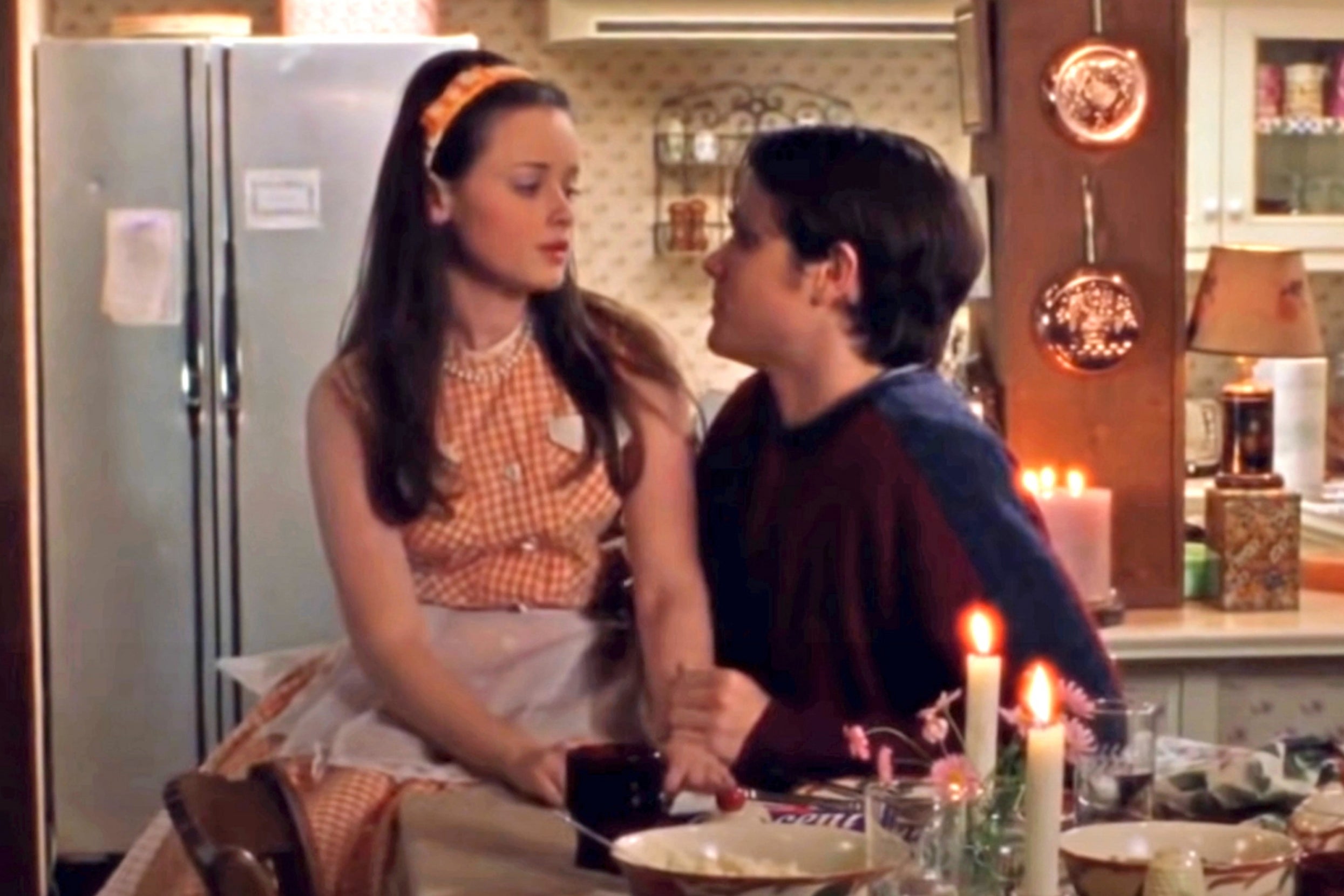 Rory and Dean from Gilmore Girls sitting in front of a table with lit candles and plates on it