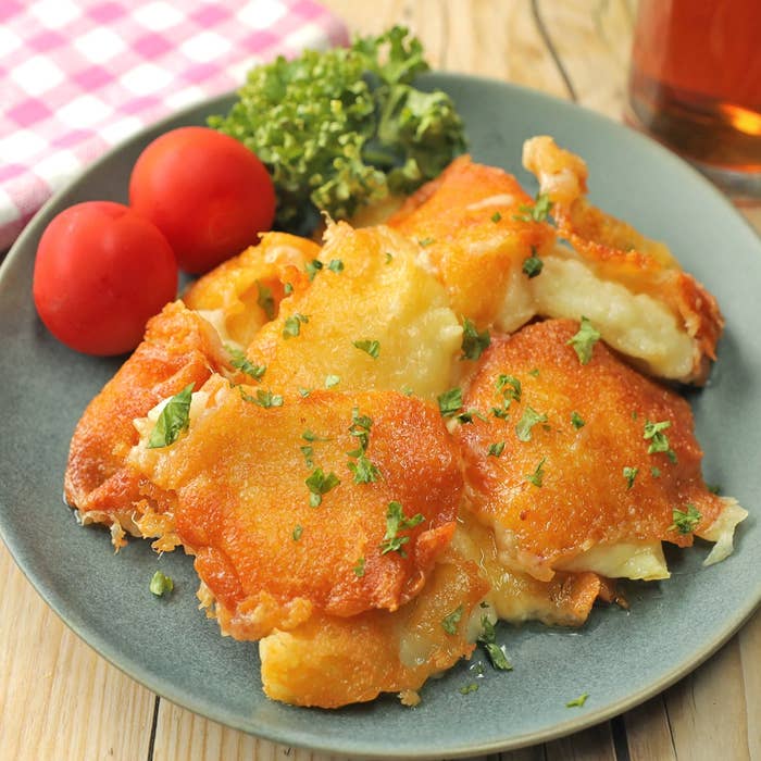 皿に盛り付けられた焼きチーズがかかった料理。横にはトマトとパセリが添えられています。