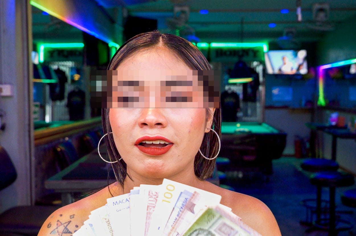 Person holding a fan of money with a thoughtful expression, in a bar setting