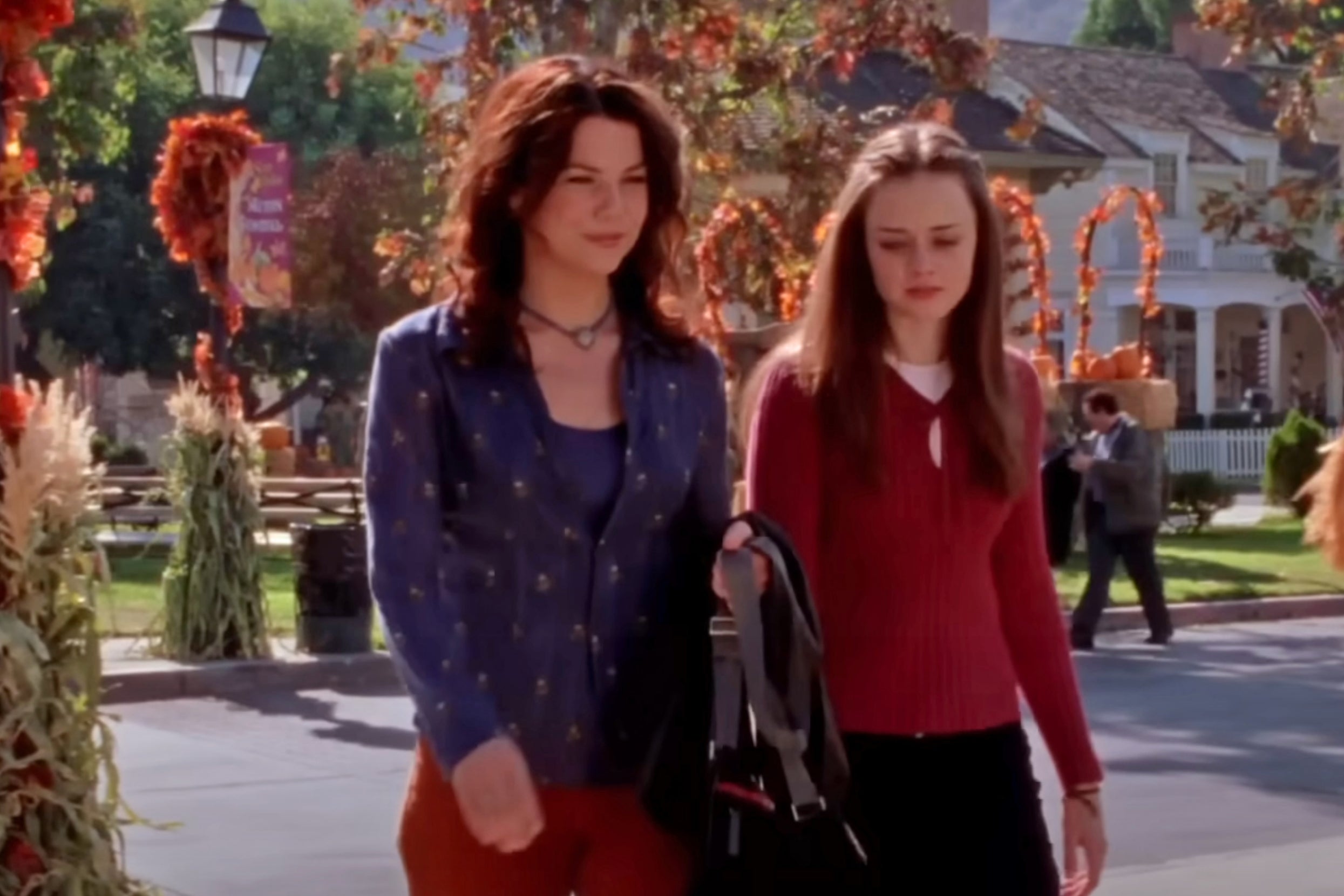 Lorelai and Rory Gilmore walking down a the street in a neighborhood decorated for fall