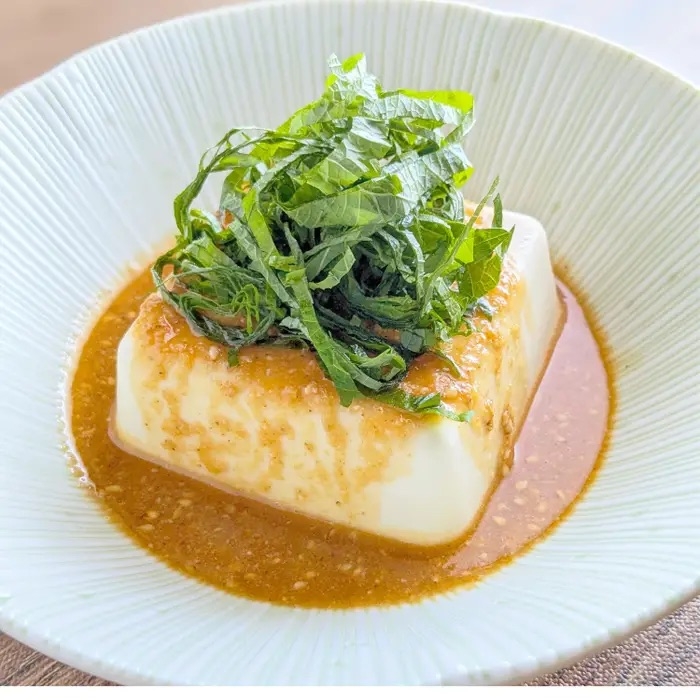 ピリ辛うまだれ豆腐。冷奴に刻んだ青じそがのっている白い皿。豆腐にたれがかけられている。