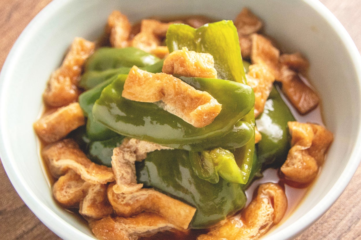 ピーマンと油揚げを煮込んだ料理が白い皿に盛られている。
