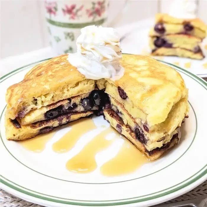 クリームが載ったパンケーキがシロップと共に皿に盛られている。パンケーキはブルーベリーが挟まれている。