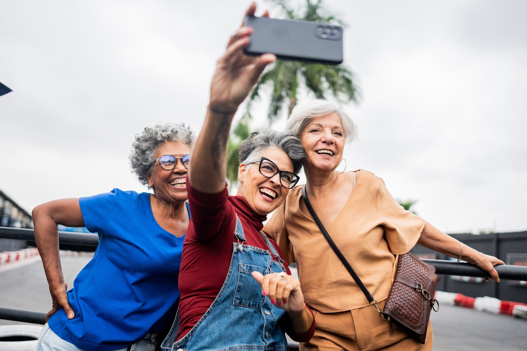 Three seniors joyfully take a selfie at an outdoor go-kart track with visible tires and palm trees in the background