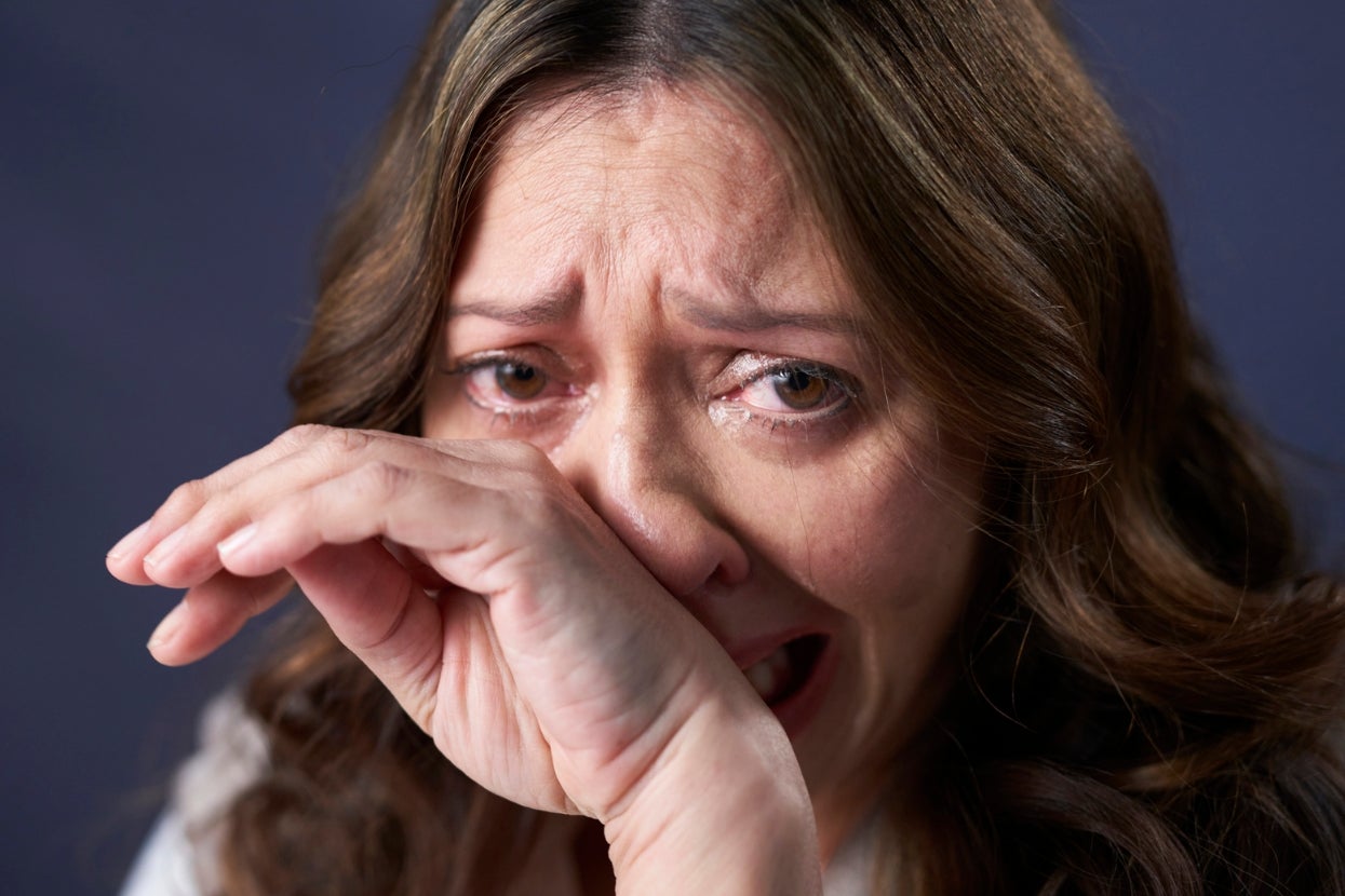 A close-up of a person with long hair, crying and wiping away tears with their hand, conveying strong emotion or distress