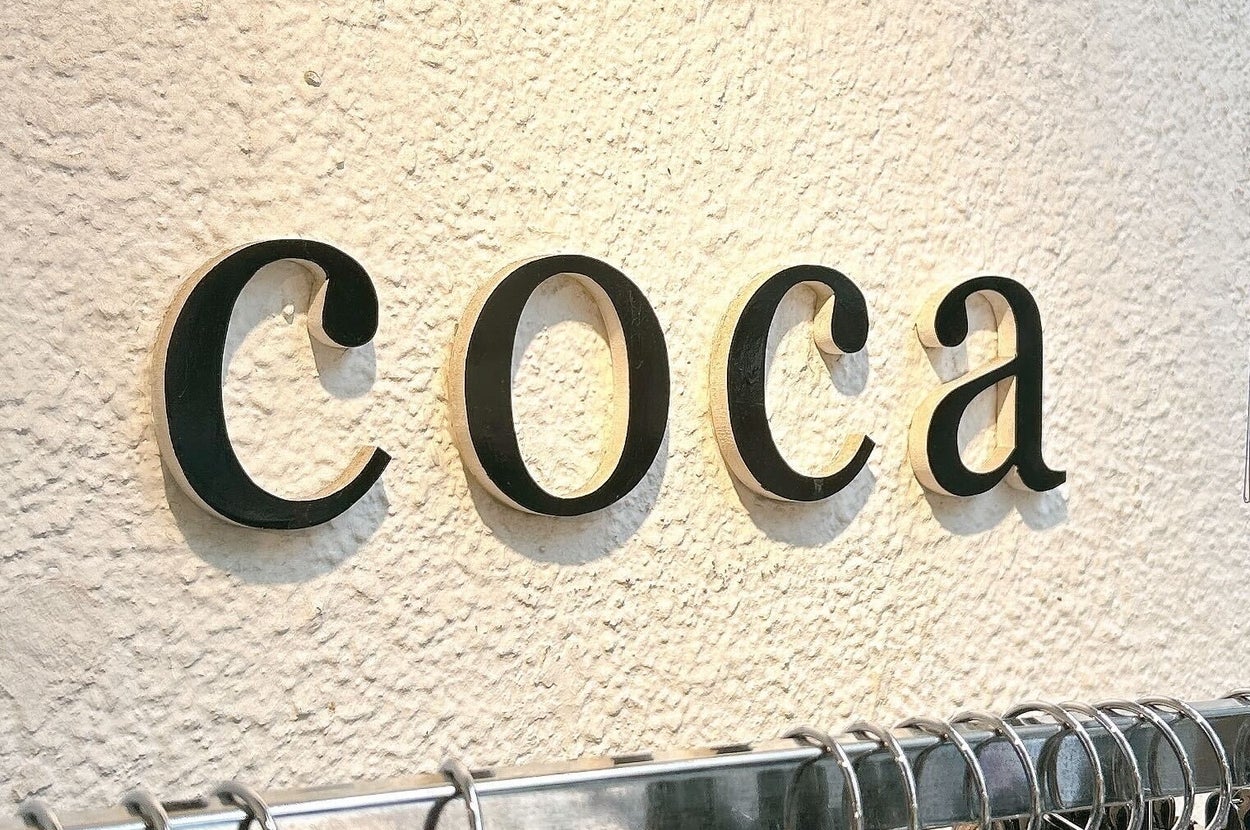 壁に「coca」と書かれた看板が掛かっており、下には洋服がハンガーに吊るされています。