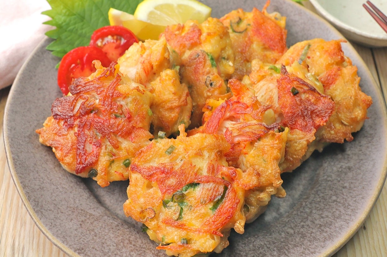 料理の盛り付け。お皿の上にかき揚げが盛られ、添えられたトマト、シソ、レモンがアクセント。