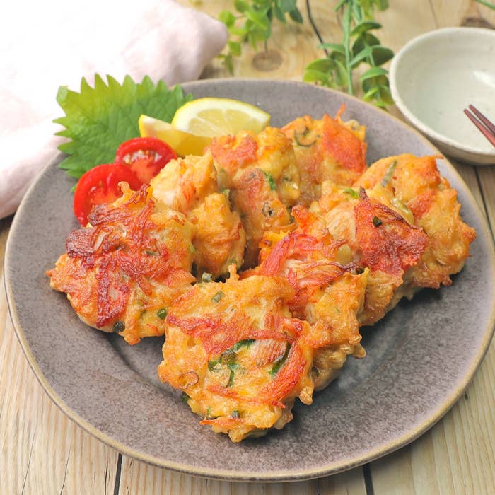 料理の盛り付け。お皿の上にかき揚げが盛られ、添えられたトマト、シソ、レモンがアクセント。