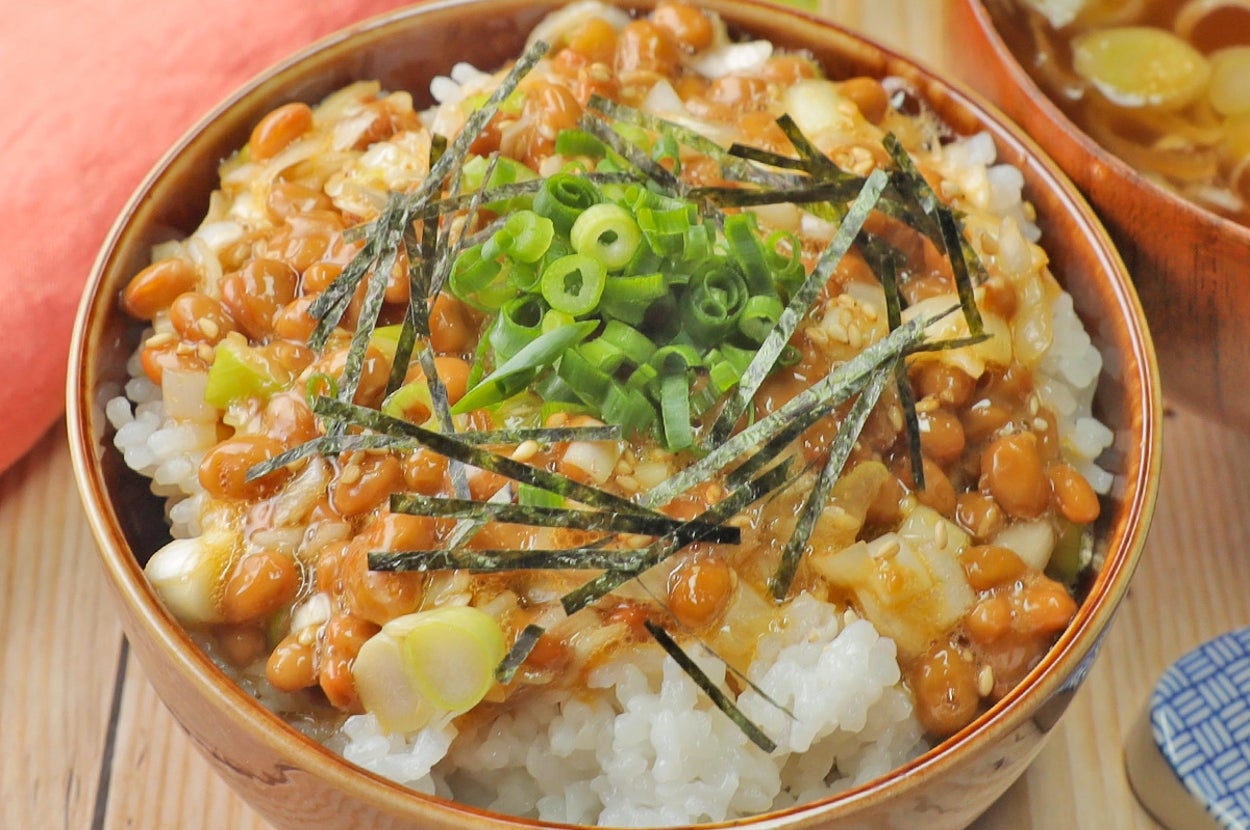 器に盛られたご飯の上に納豆、刻み海苔、ネギが載っている。隣に味噌汁が見える。