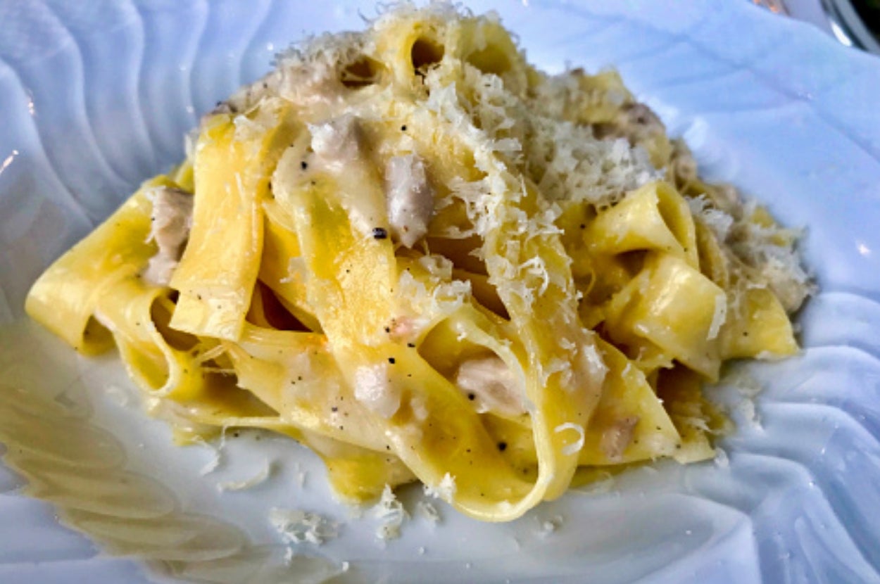 A plate of fettuccine pasta with creamy sauce and grated cheese on top, served on a decorative plate