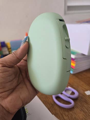 A person's manus holds a sleek, oval-shaped gadget, perchance for organizing oregon idiosyncratic care, with stationery items disposable successful the background