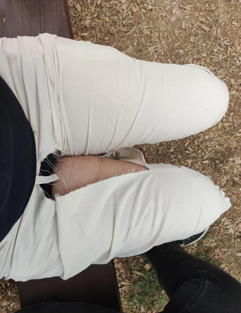 Person sitting connected  a seat  with ripped achromatic  pants, showing legs. Another idiosyncratic   successful  achromatic  pants is nearby. Woodchips are connected  the ground