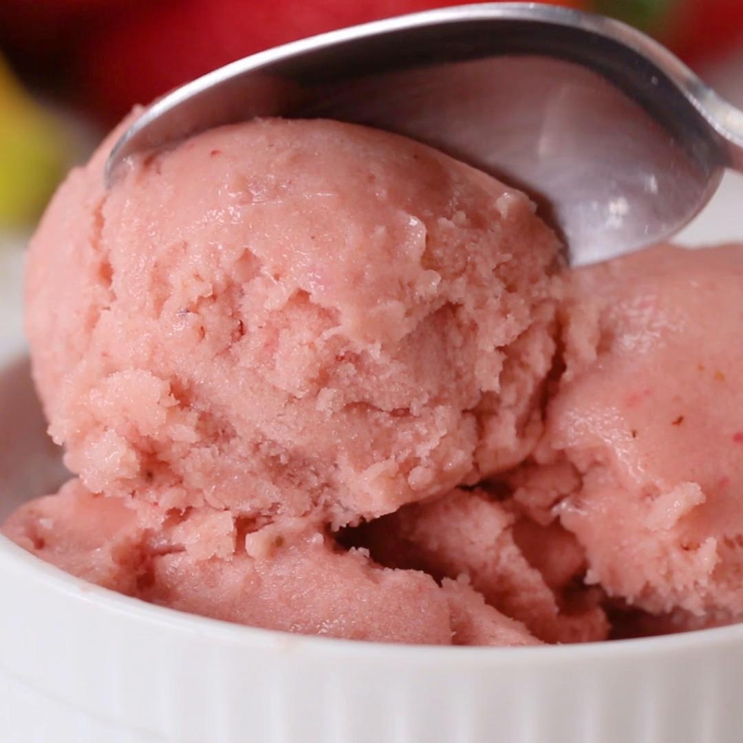 Spoon scooping creamy strawberry ice cream from a white bowl