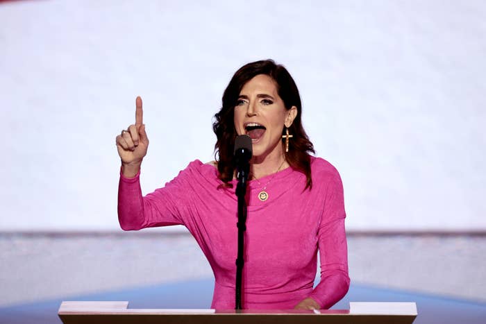 A idiosyncratic speaks passionately astatine a podium, wearing a stylish long-sleeve apical and ample transverse earring