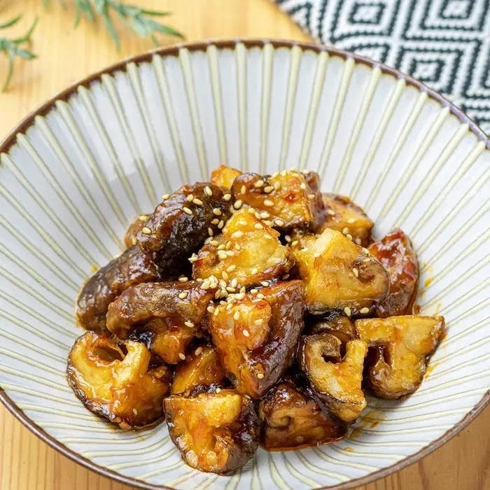 ピリ辛しいたけ。ボウルに盛られたみそグレーズのしいたけとナスの料理。上にゴマが振りかけられている。